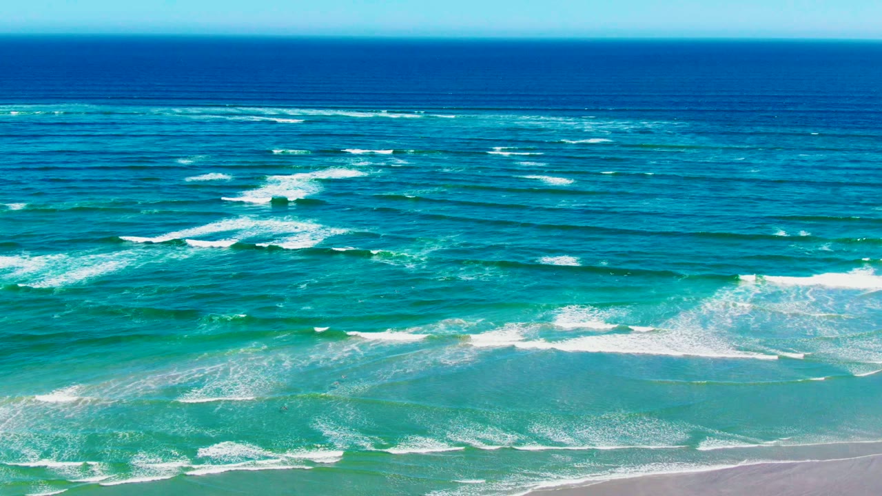 White wave crests crossing turquoise water toward sand.