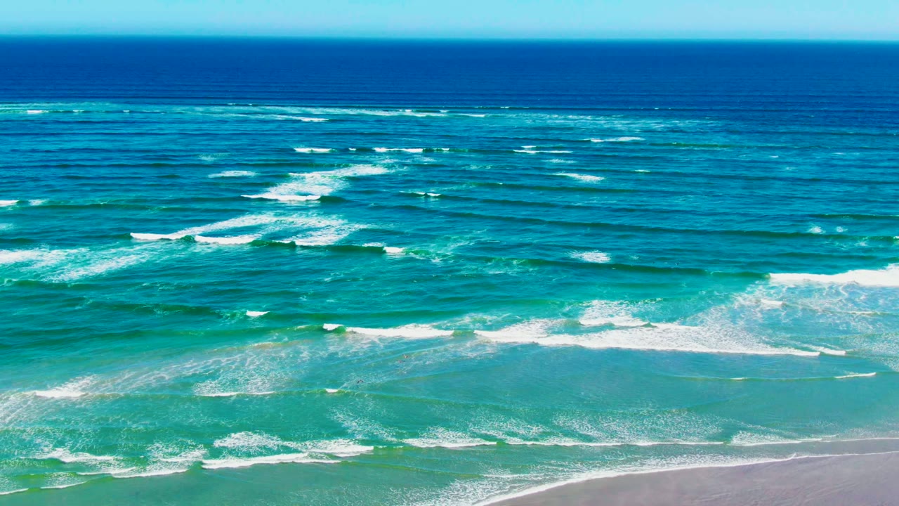 At La Bocana, scattered white foam bands sit over green-blue surf with the sandy beach visible along the lower edge and no visible people.