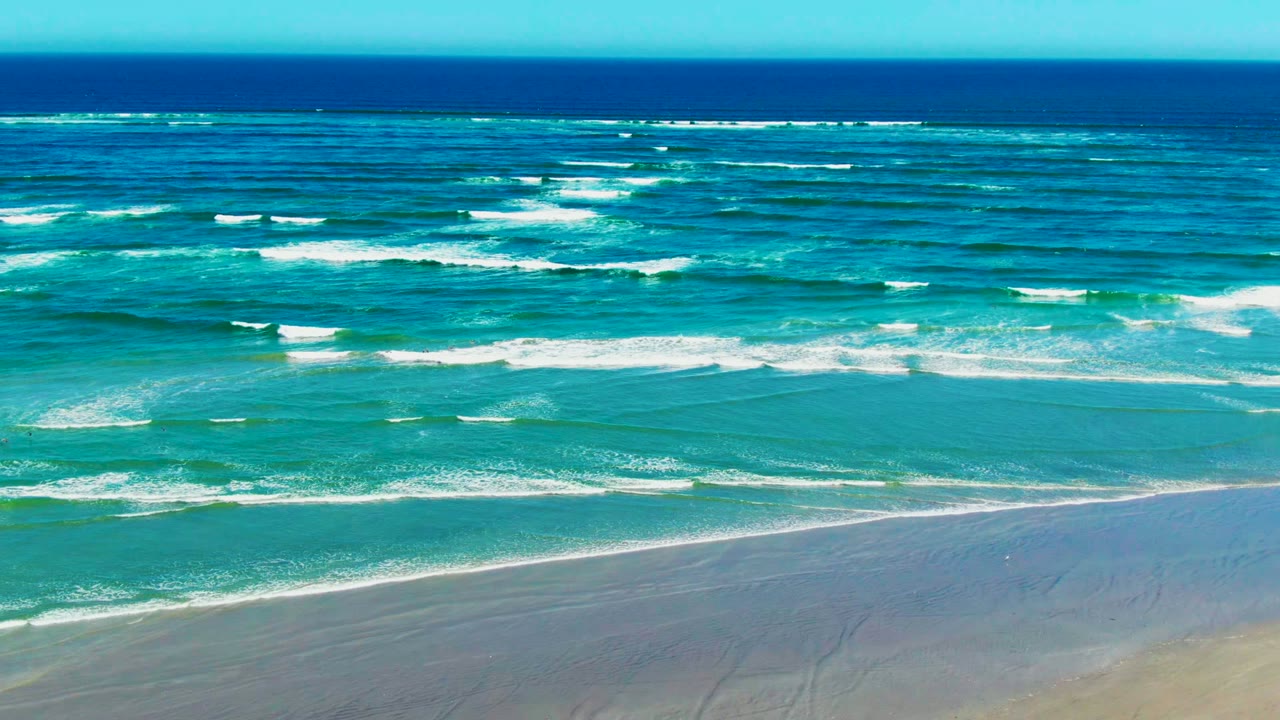 Turquoise waves breaking in rows before a sandy shoreline