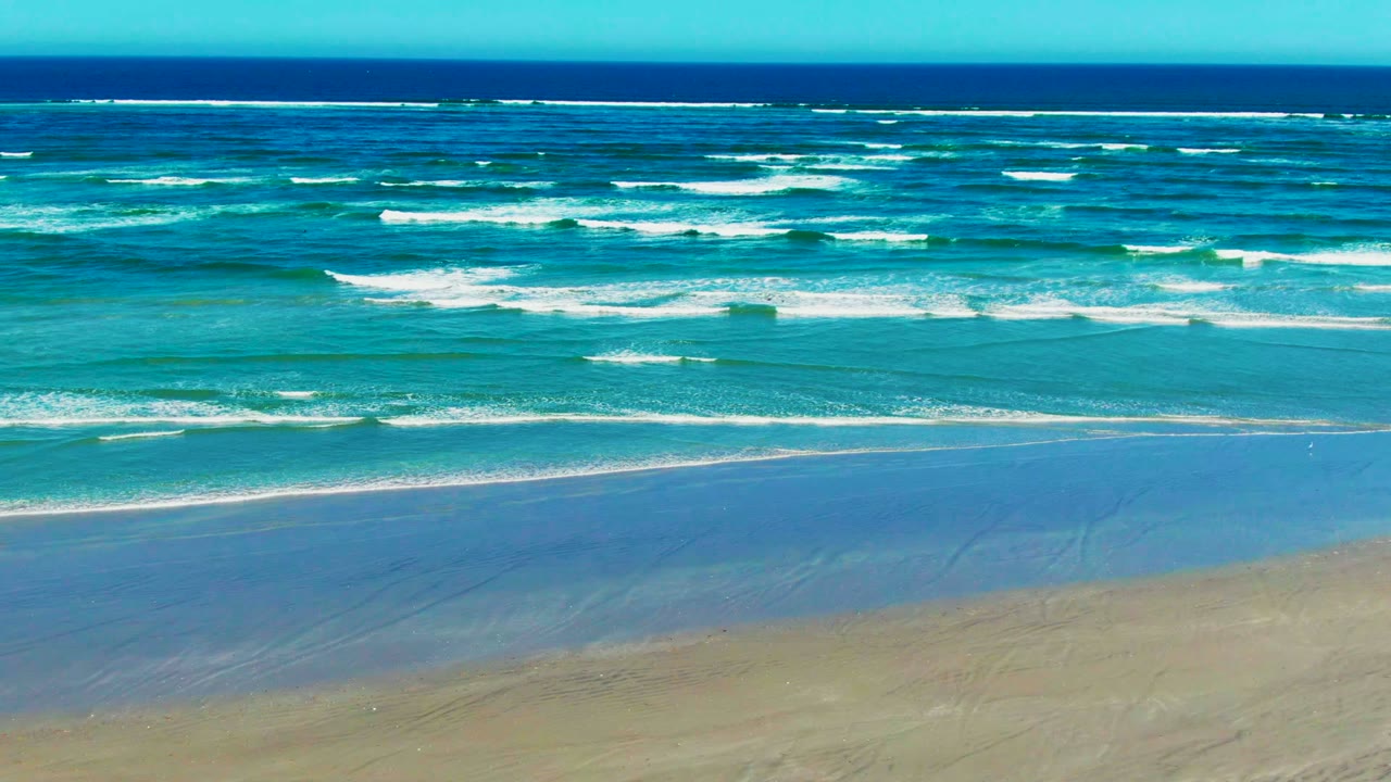 Sandy shore with white surf lines across turquoise water