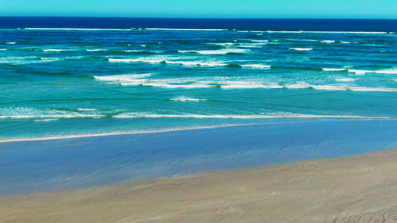 Turquoise water approaches the La Bocana sand while white foam breaks across the midground and the darker ocean sits near the horizon, with no visible people.