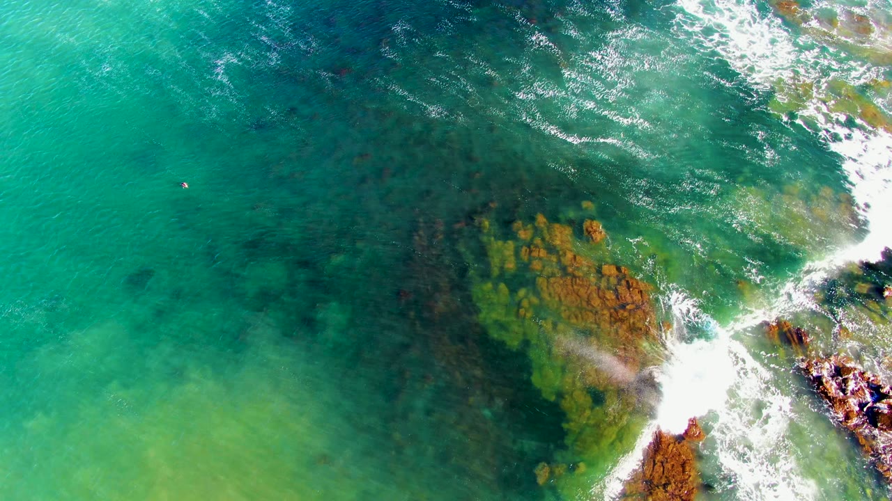 Clear green-blue water breaking over coastal rocks