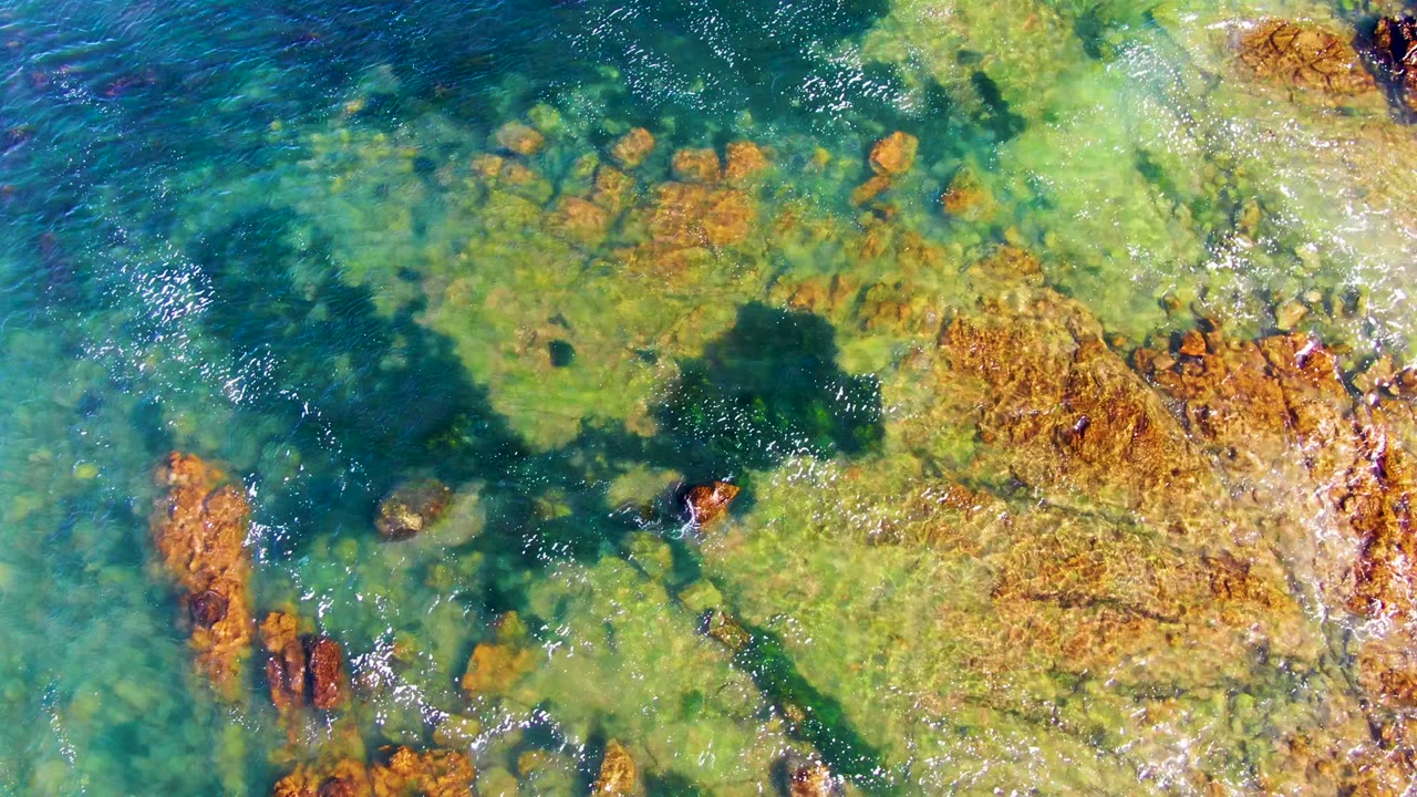 Aerial view of rippled clear water crossing a rocky seabed.