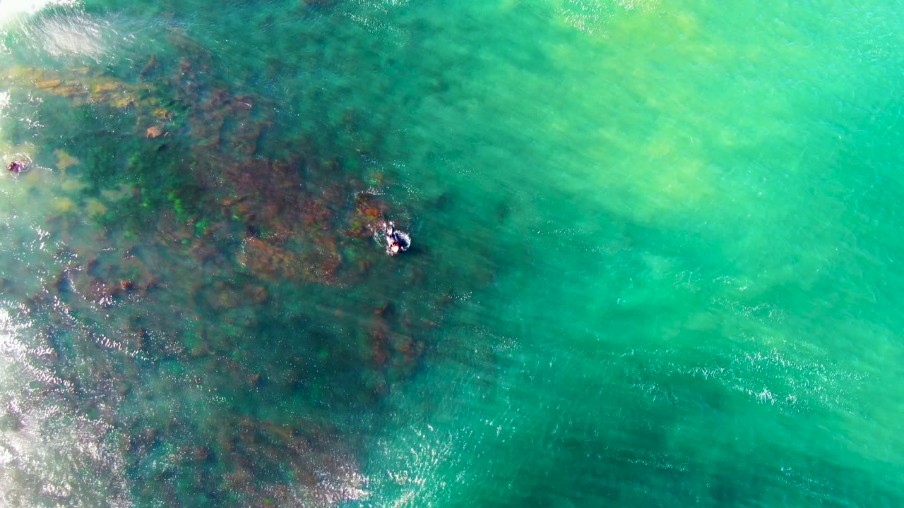 Overhead La Bocana surf view with the surfer near the upper middle-right, reef-dark water filling the left side, and bright turquoise water opening across the right.