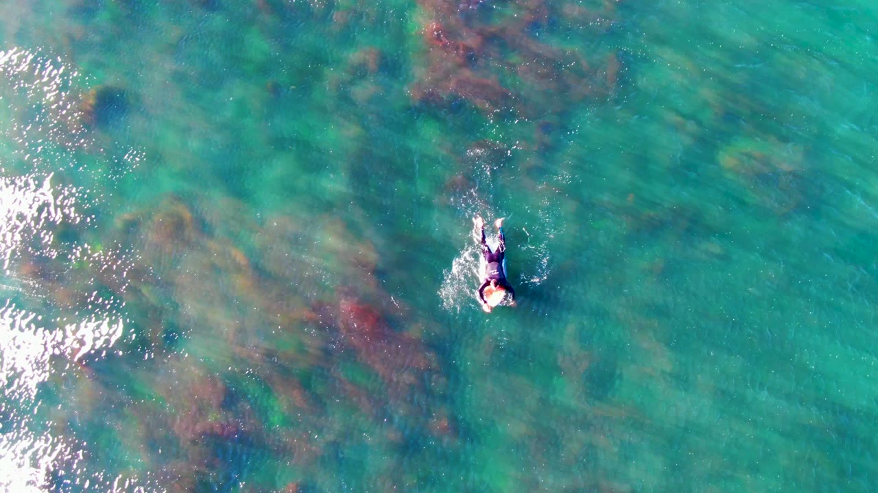 Overhead view of the swimmer in La Bocana's turquoise ocean water, with bright white wave reflection and foam entering along the left edge.