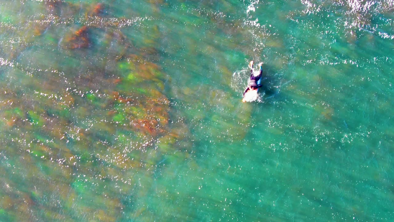 Small swimmer moving through clear green-blue water above submerged rock patches.