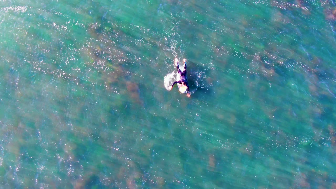A single swimmer is viewed from above in rippled turquoise water at La Bocana, Mexico, with their arms and legs visible and no shoreline in frame.
