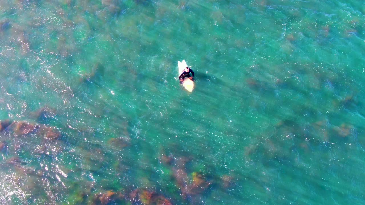 Person on a board seen from above in clear blue-green ocean water.