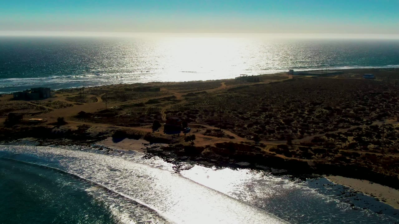 Sunlit ocean and waves along a rocky sandy coastline