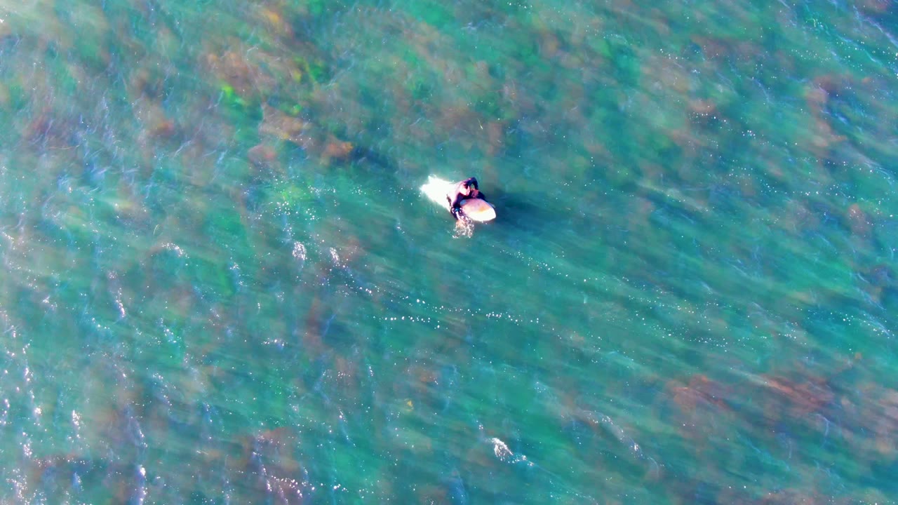 Surfer paddling on a light board over blue-green water.