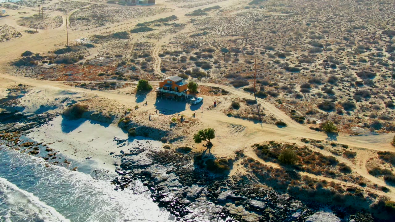 Drone view of surf hitting rocks below a small desert house