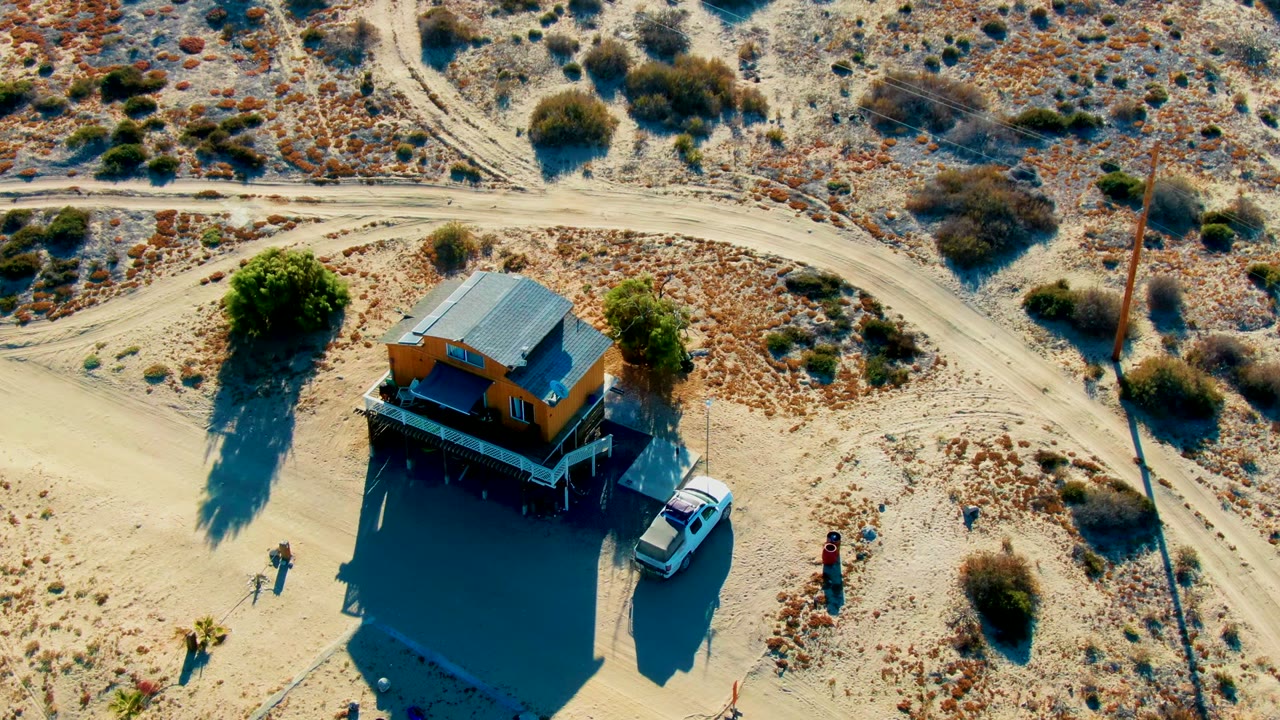 Aerial view of the desert house with a white car and people near the sandy lot.
