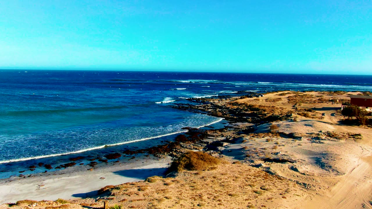Blue ocean and sandy rocky coastline seen from an elevated angle.