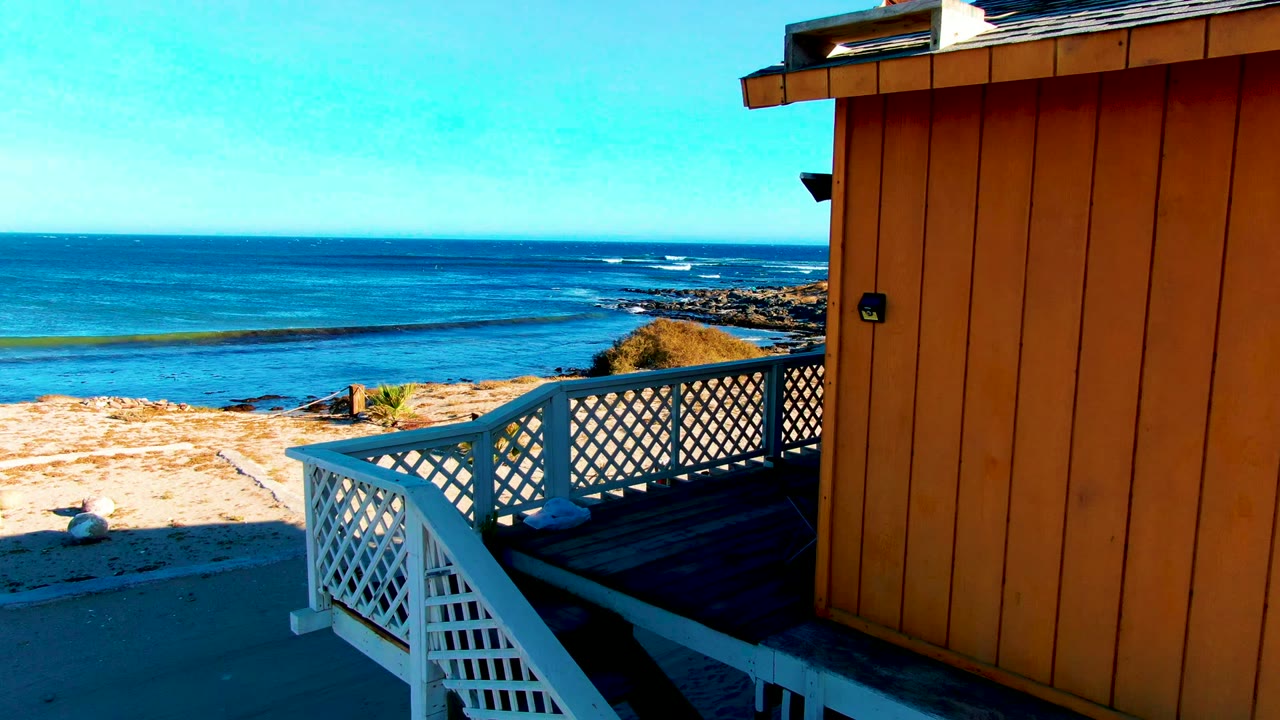 White deck railing beside orange beach house with ocean beyond