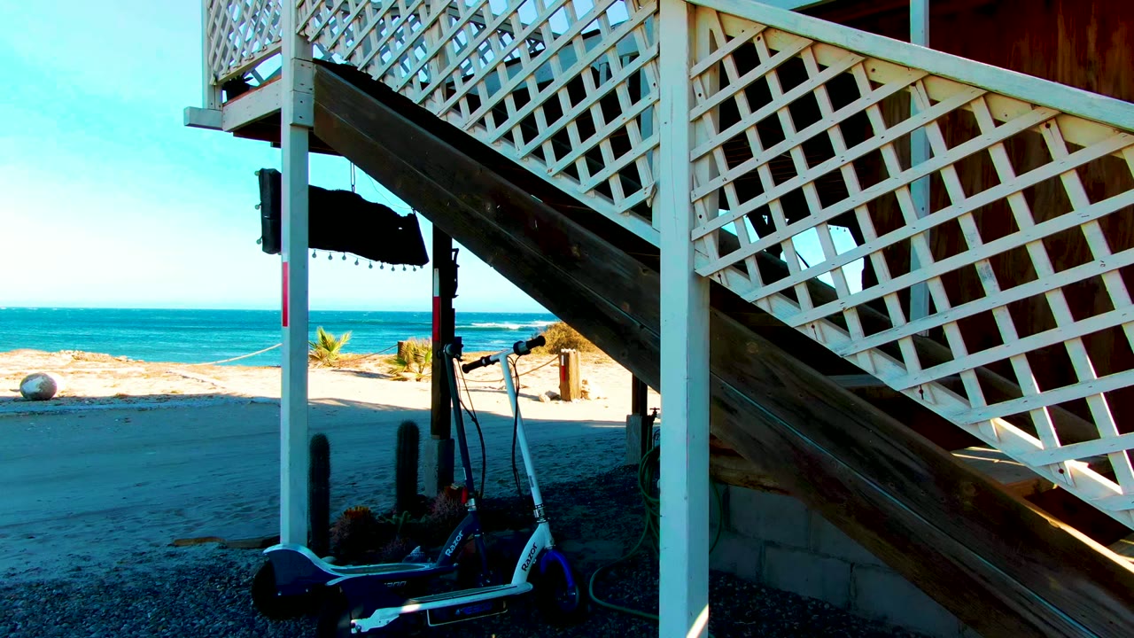 Closer view of white lattice staircase with ocean and scooter below.