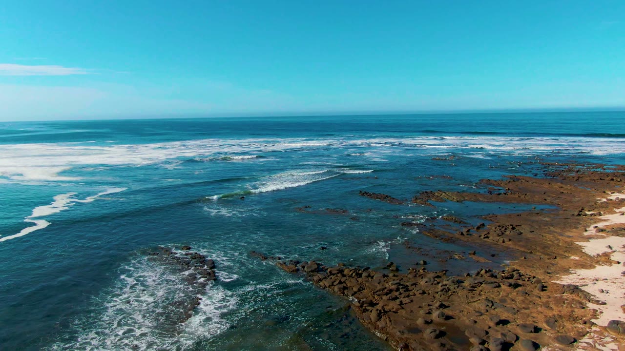 White surf curls toward dark rocks beside exposed reef shelves