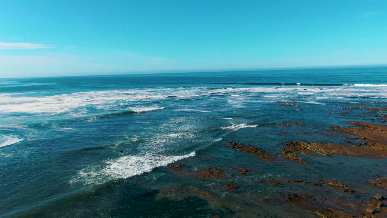 White wave foam advances across blue water and brown rock shelves.