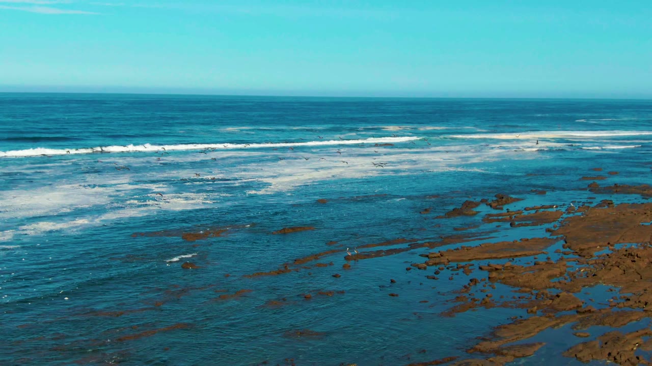 Wide ocean horizon with surf rolling across exposed coastal rocks