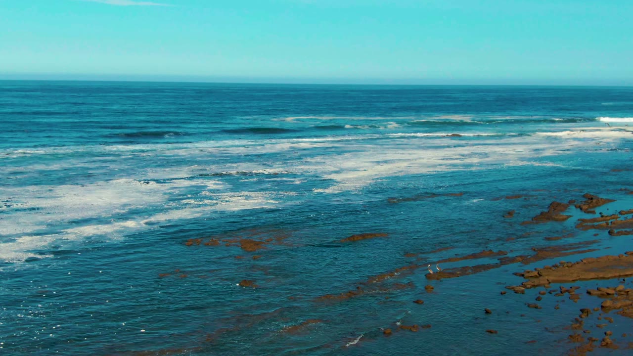 White foam spreads across blue water above exposed rock shelves.