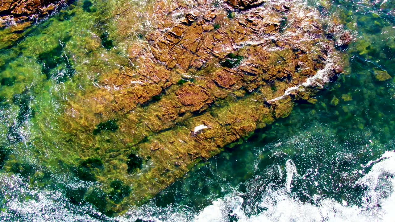 Clear green water laps across angled brown rock shelves.