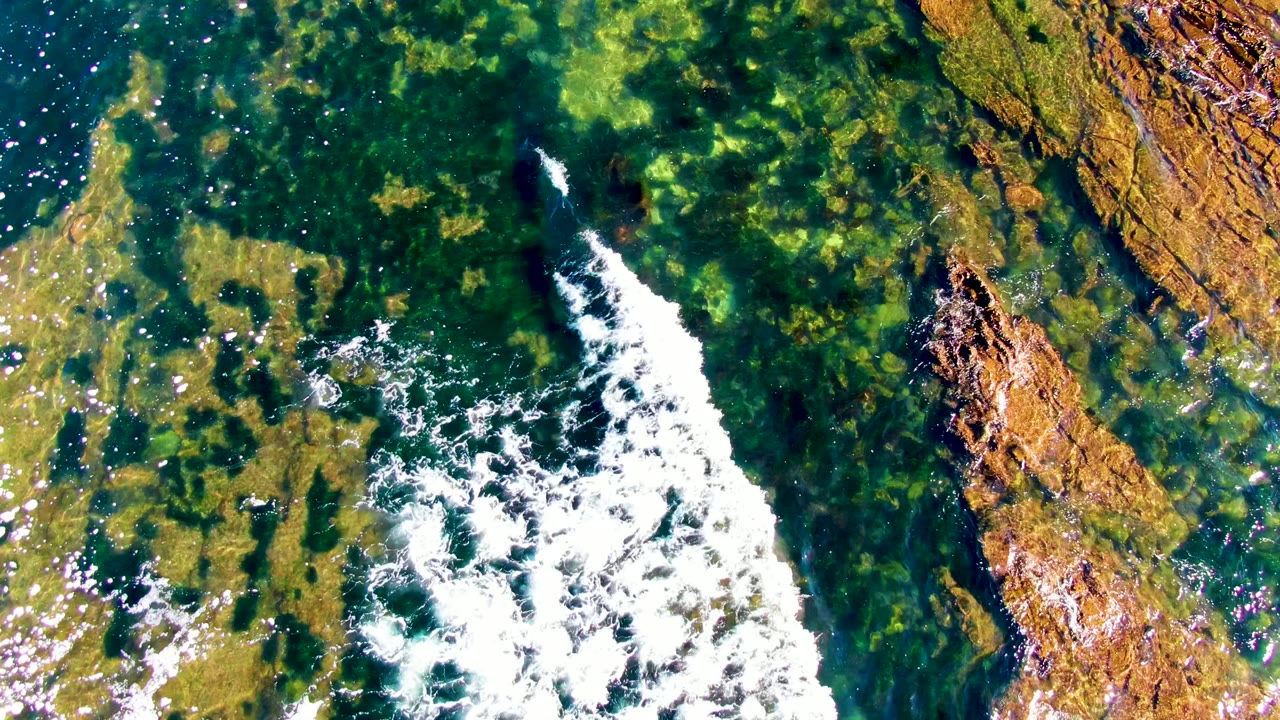 White surf crossing shallow green water and rock shelf