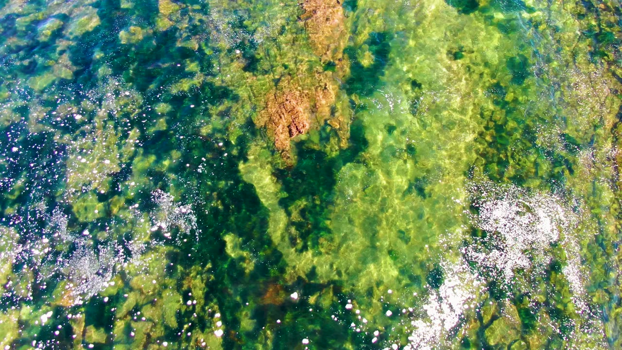 Green-blue water over submerged rocks with bright glints