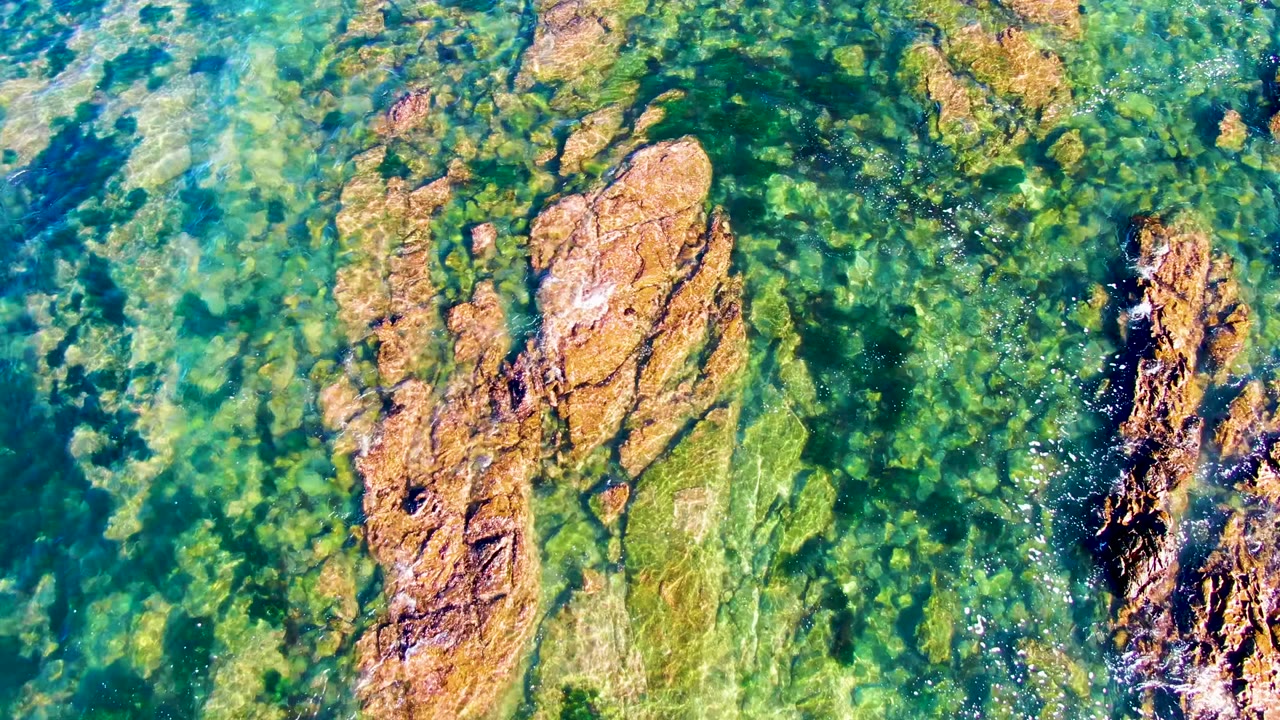 A top-down La Bocana view shows two prominent orange-brown rock formations surrounded by transparent green water, algae patches, and no visible people.