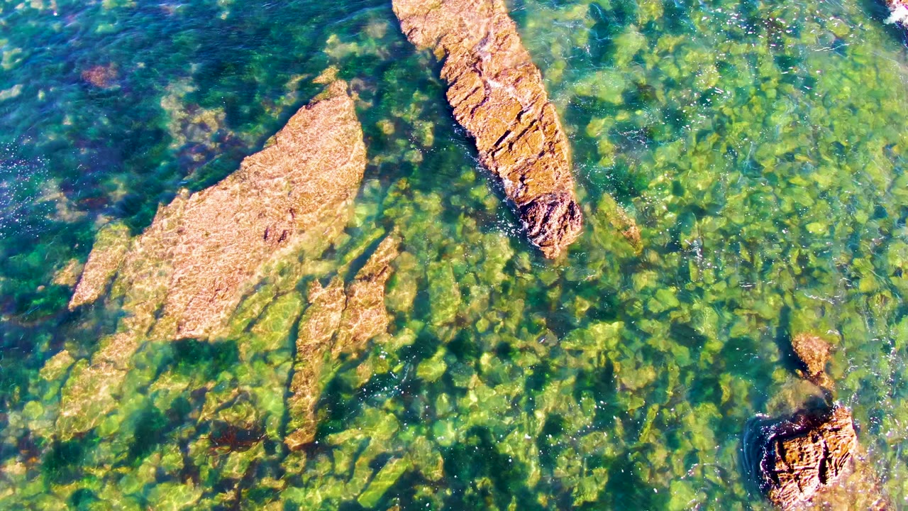 Clear water surrounds a broad rock shelf and narrow rock ridge.