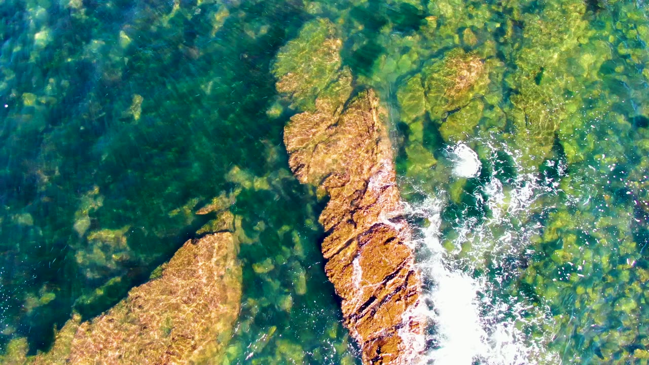 Clear shallow ocean water with a central tan rock and foam streaks.