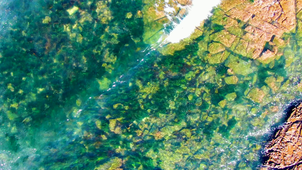 Shallow clear water with rocks below and white foam near the upper edge.