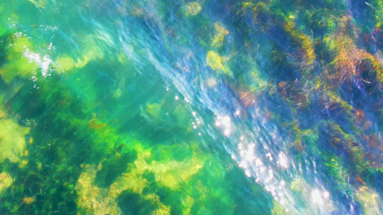 A brighter wave-disturbed area crosses the clear turquoise water over algae and pale bottom in La Bocana, with no visible people.