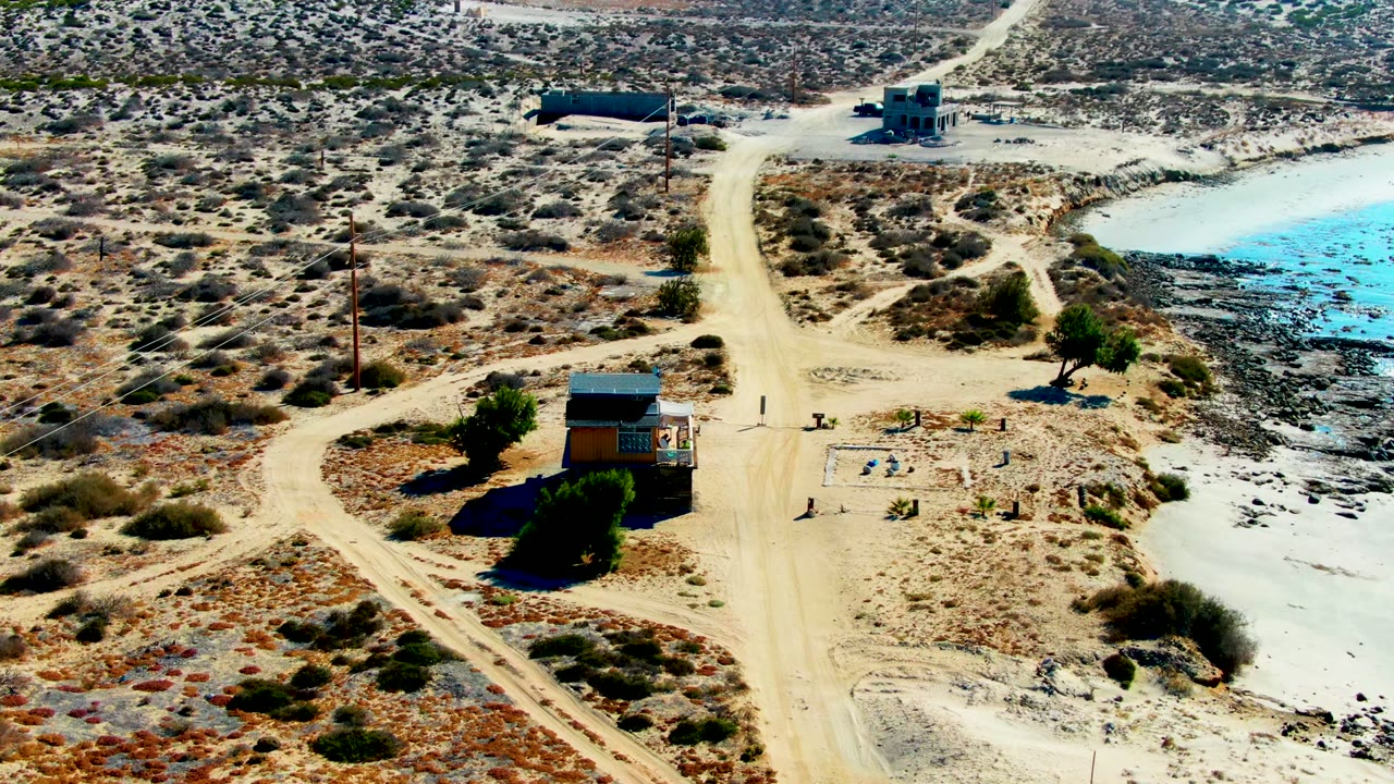 Drone view moving closer to a small cabin beside scrub and a reservoir.