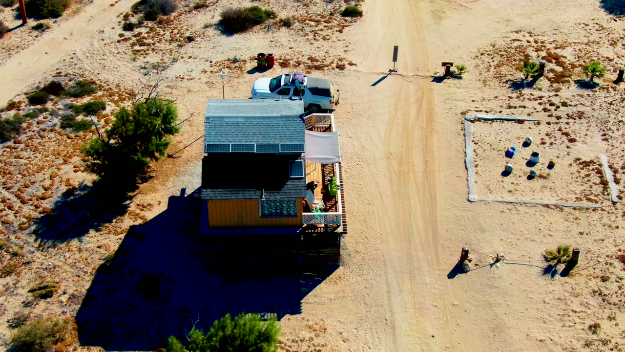 White truck approaching a desert house beside a sandy road.