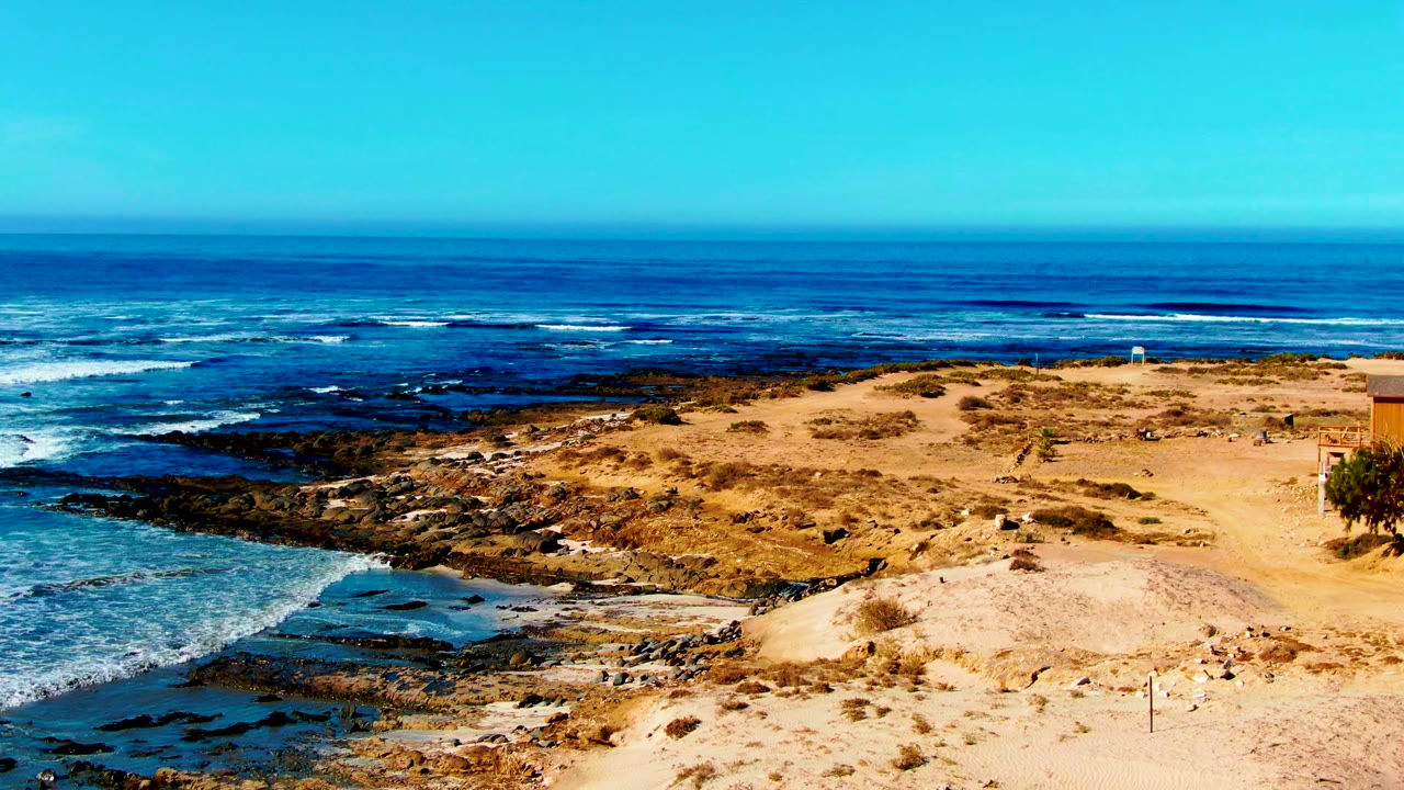 Sandy bluff above dark rocks with waves breaking offshore.