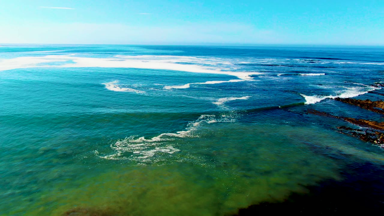 White waves curve across blue green water beside dark rocks