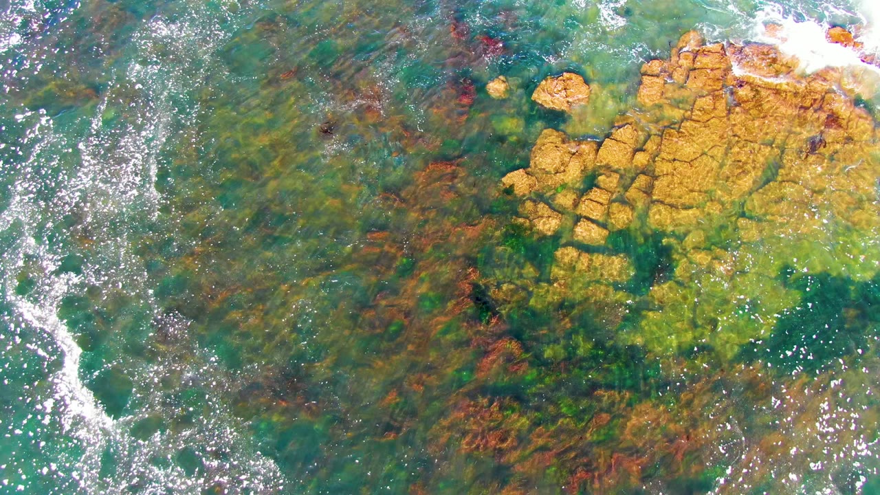 White foam curves beside submerged rocks in green-blue water.