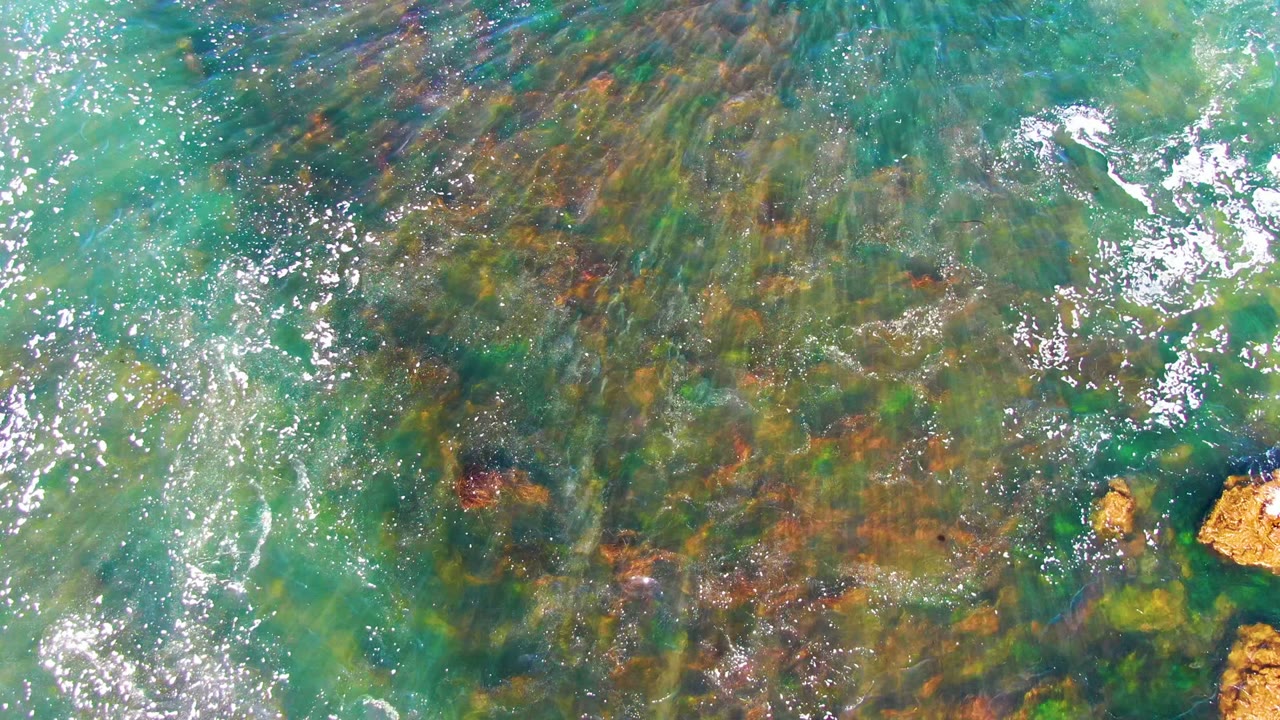 Clear green-blue ocean water with foam streaks over rocks