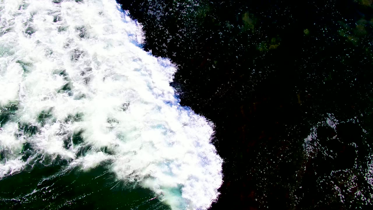 Overhead view of white surf foam pushing across dark green ocean water in La Bocana, Baja California Sur, with no visible people.
