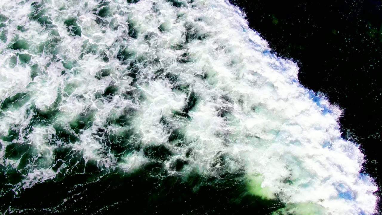 Broad white foam sheet spreading across green ocean water.
