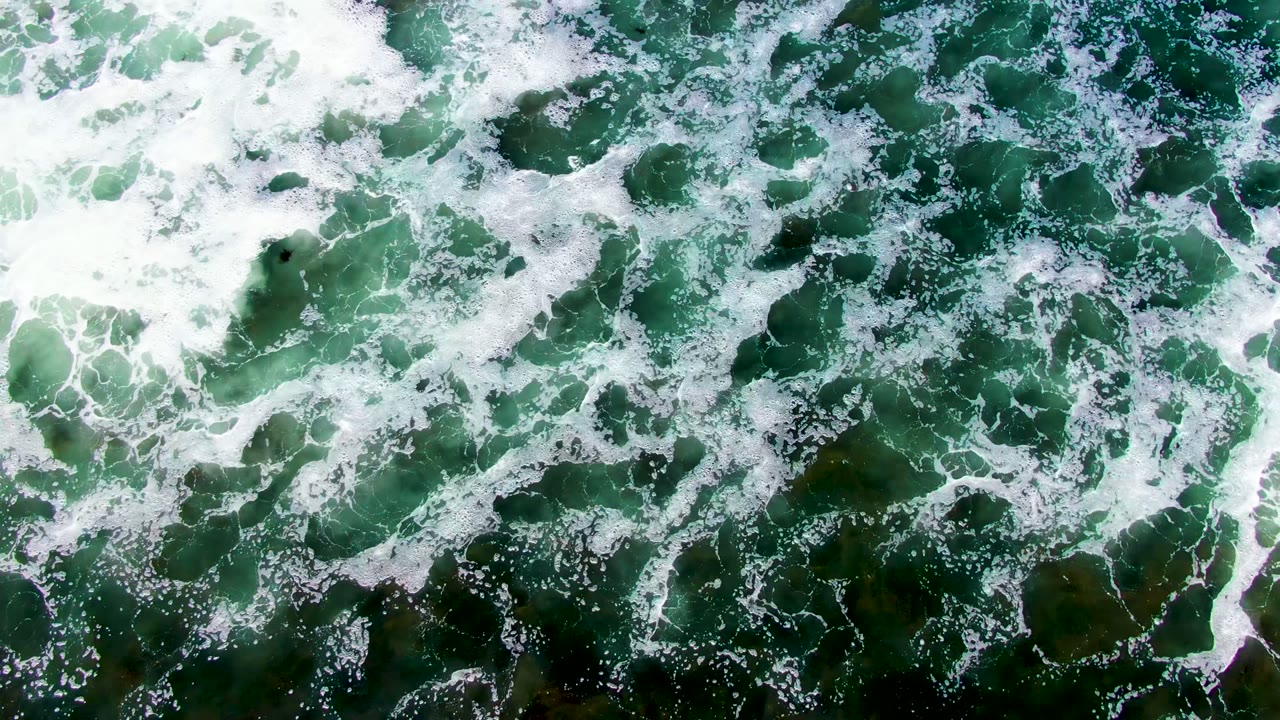 Breaking white surf thins across dark green water in La Bocana, revealing more submerged color and texture with no visible people.