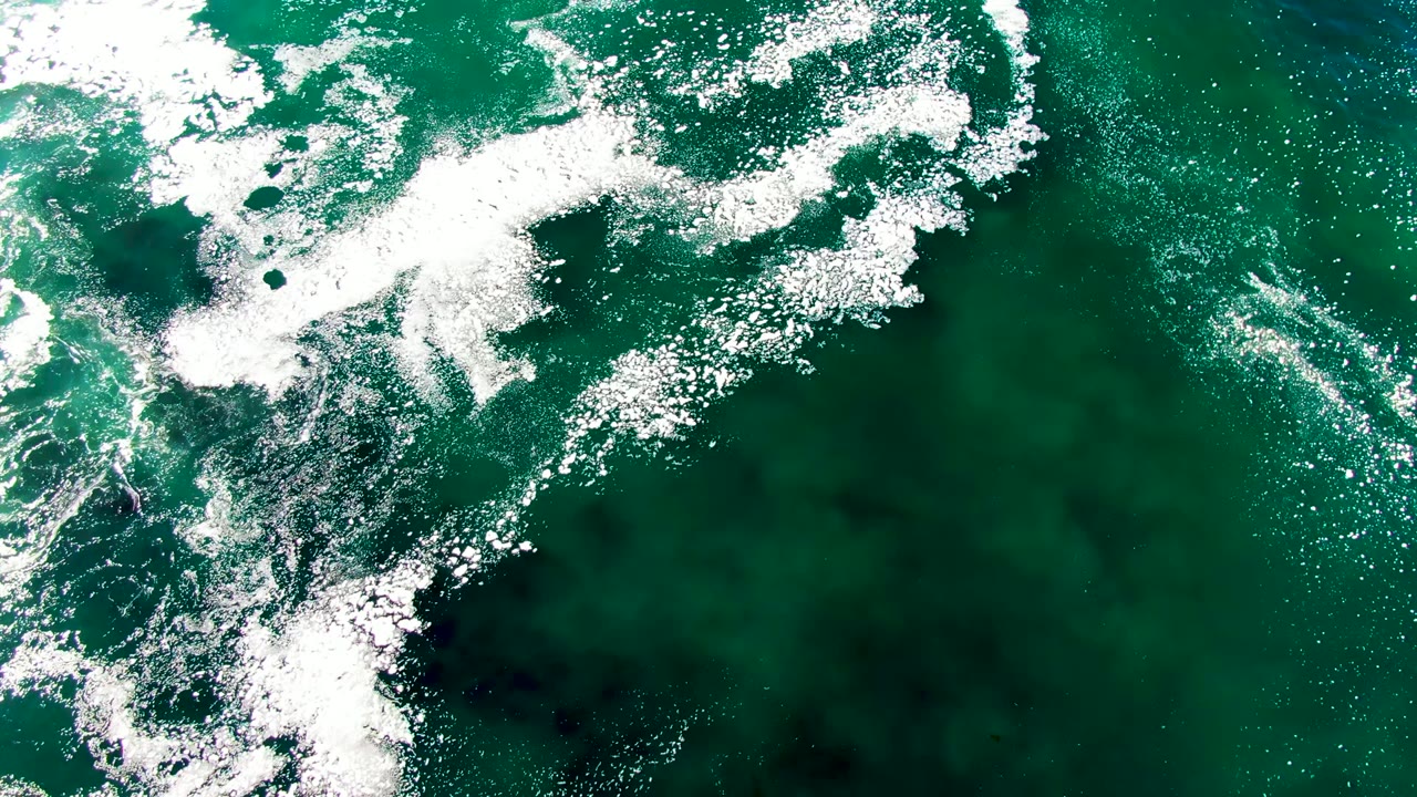Overhead view of green ocean water at La Bocana, Baja California Sur, with white foam spread across the upper left and no visible people.