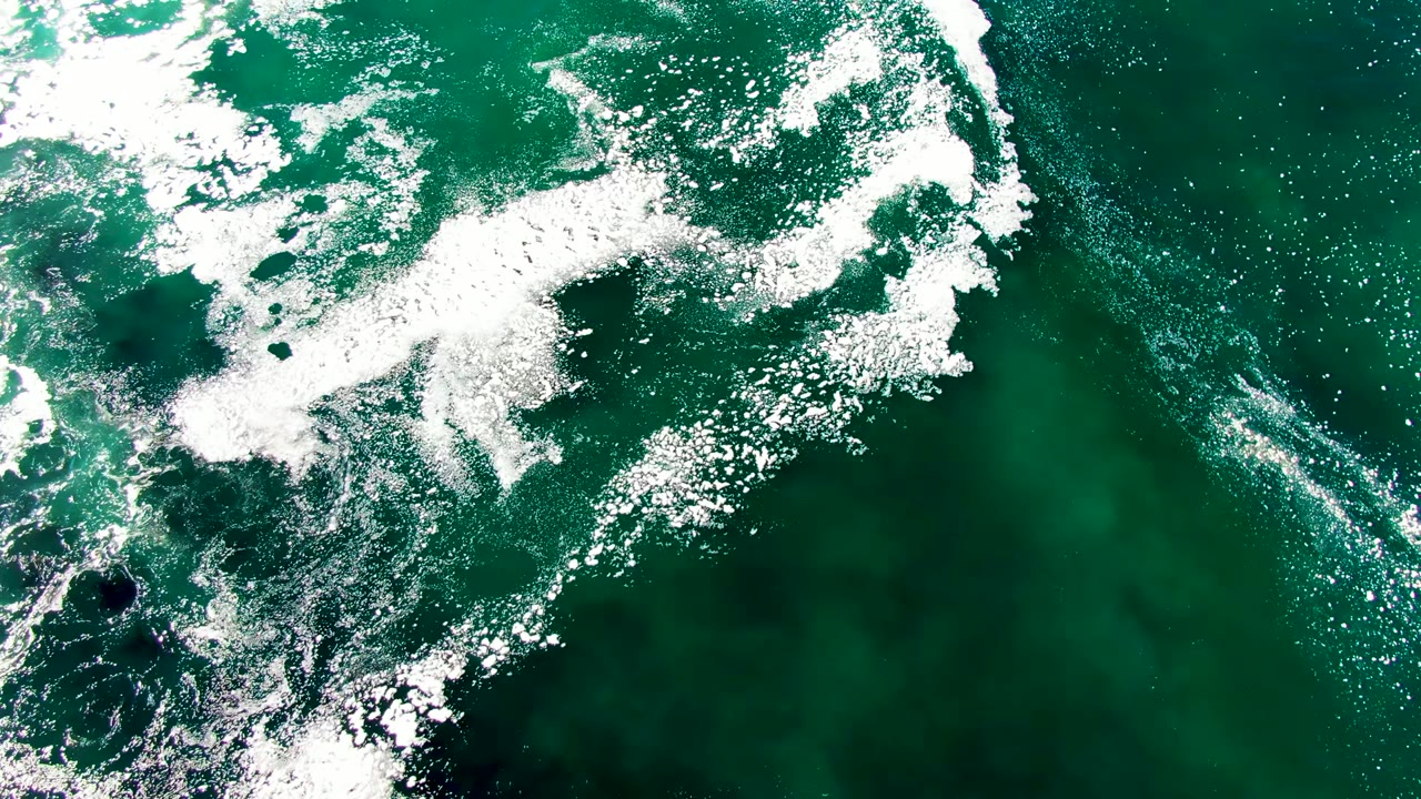 Top-down view at La Bocana with a broad white foam mass crossing green water and darker submerged areas visible beneath, no visible people.
