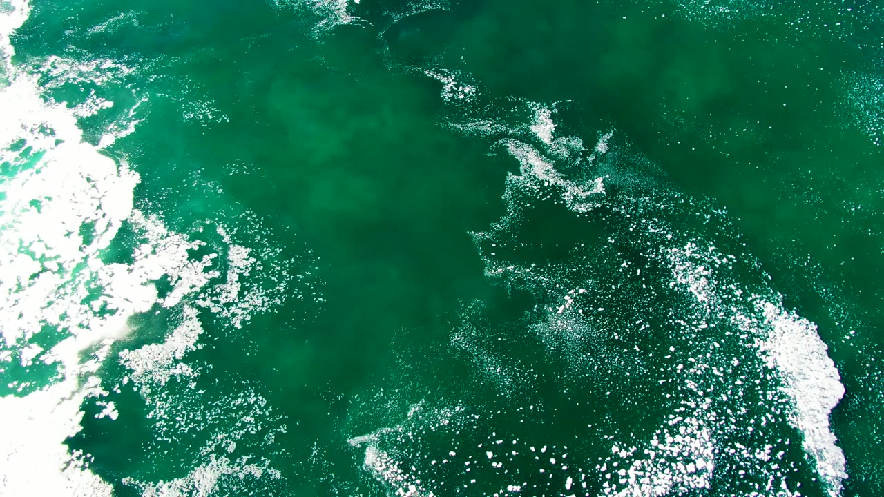 Overhead view of green-blue ocean water at La Bocana with white foam breaking through the left side and no visible people.