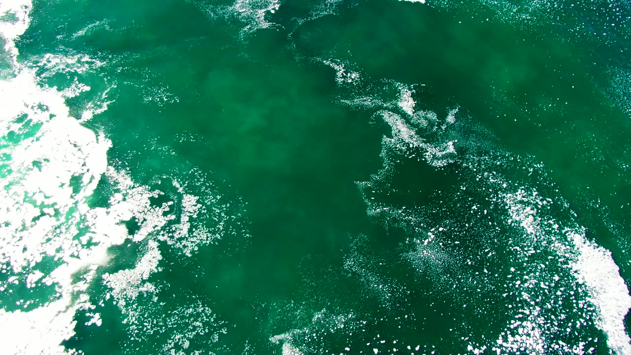 White foamy wave streaks across green ocean surface from above.