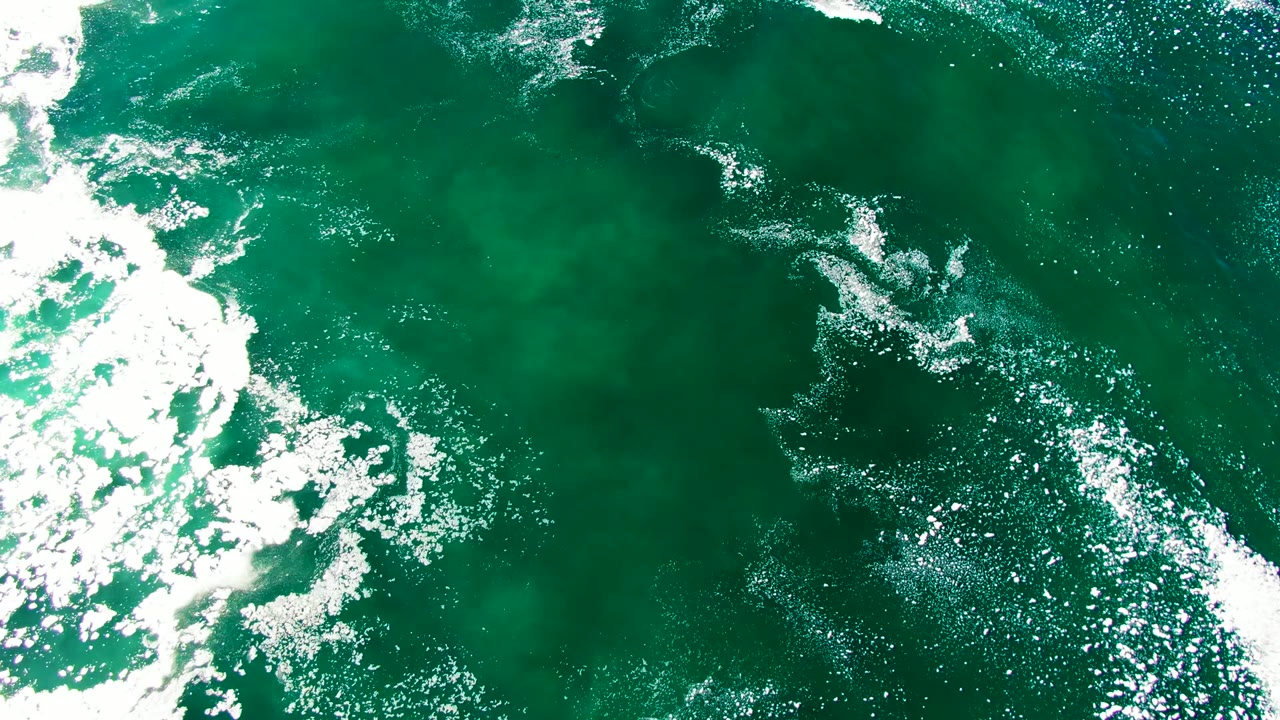 High overhead La Bocana ocean frame with scattered white foam, darker green water patches, and no visible people.