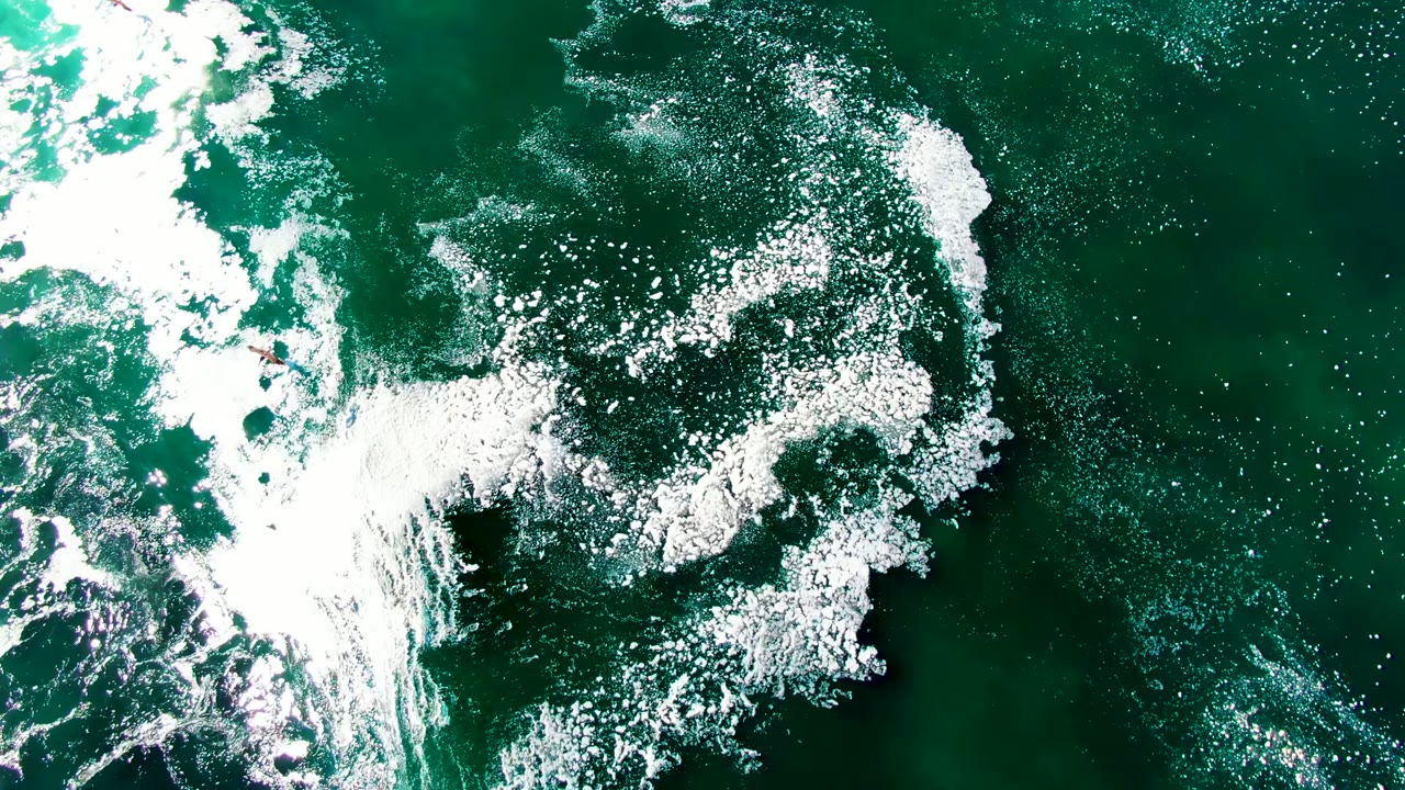 Top-down view of white surf foam spread across green ocean water in La Bocana, Baja California Sur, with no visible people.
