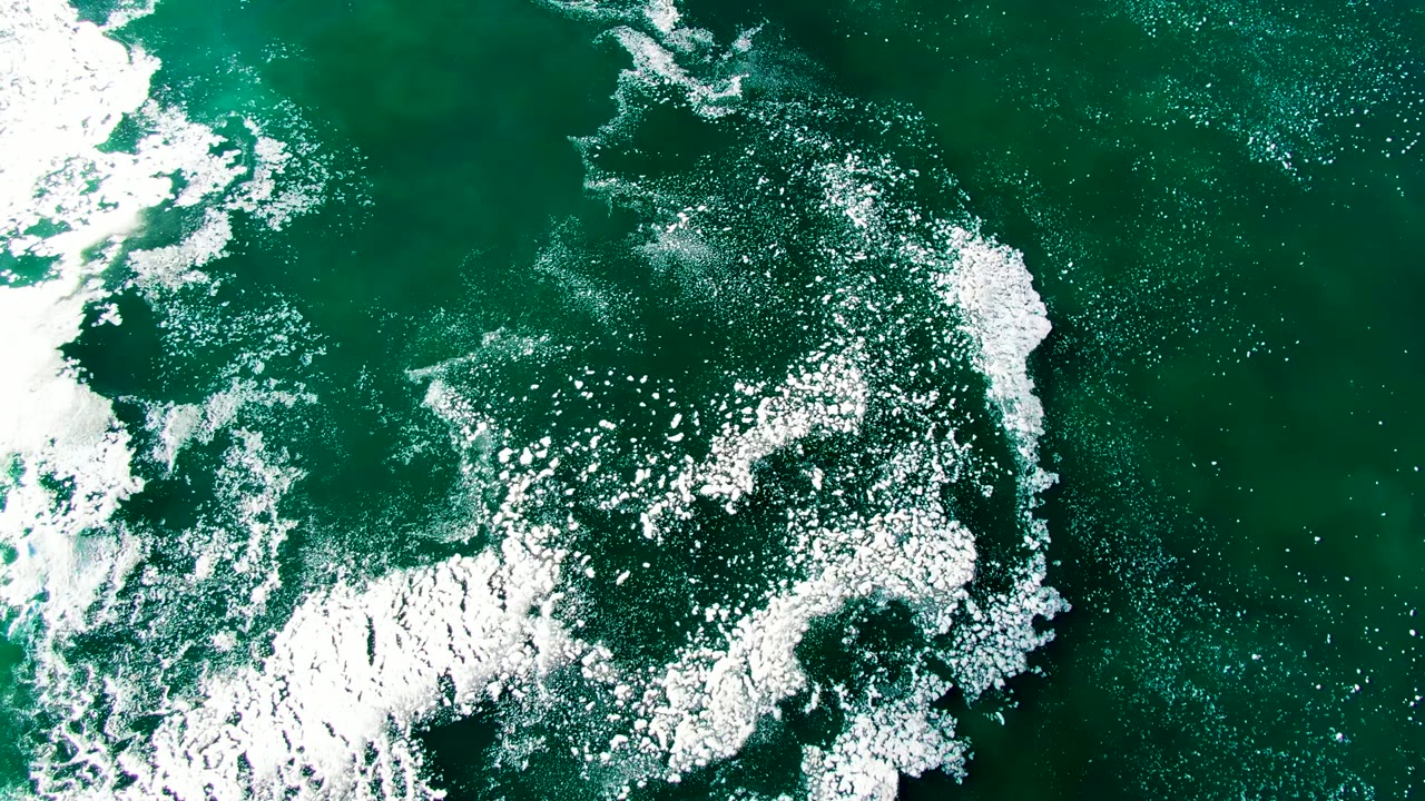 Curving white foam and fine bubbles sit over dark green ocean surface in La Bocana, Baja California Sur, with no visible people.