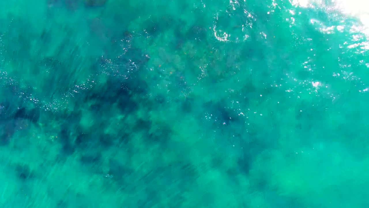 Top-down view of turquoise ocean water in La Bocana, Baja California Sur, with dark submerged patches and no visible people.