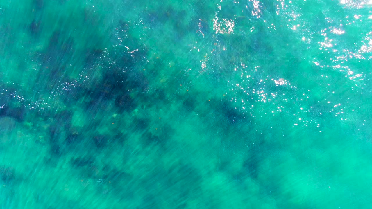 Clear turquoise water with bright sun sparkle near the upper edge.