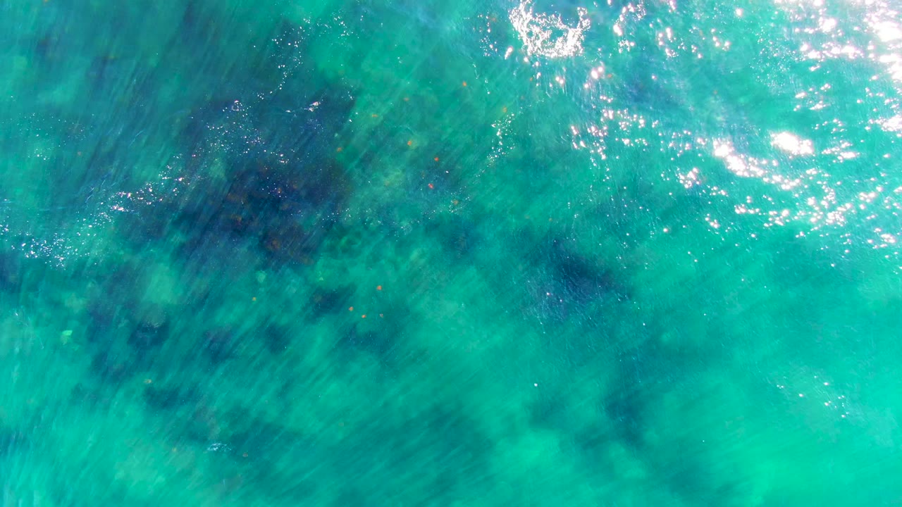 Top-down La Bocana ocean frame with turquoise ripples, scattered white reflections, and darker blue-green underwater patches, no visible people.